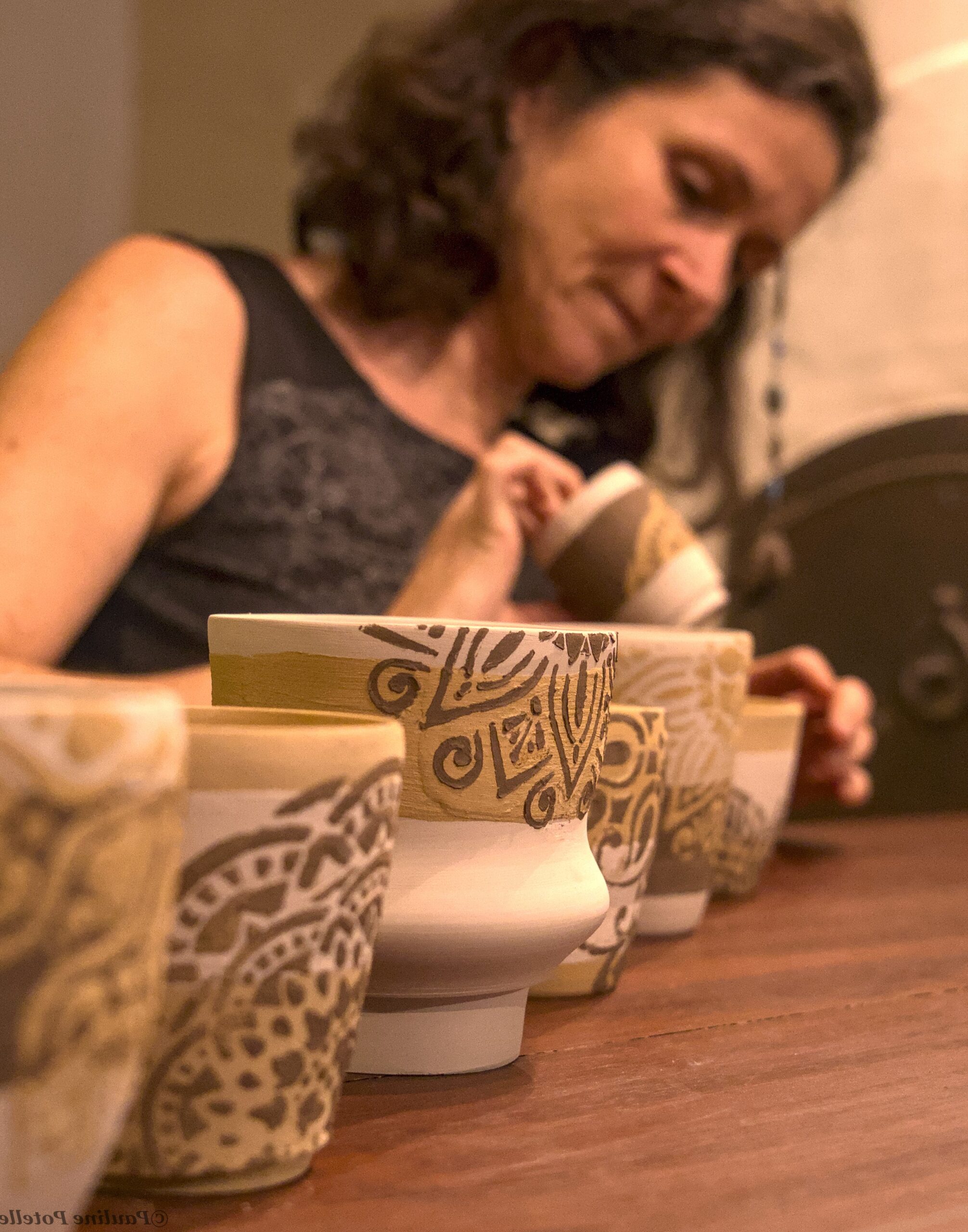 Une femme en arrière fond est en train d'aligner ses poteries blanches recouvertes de dessin mandala. 