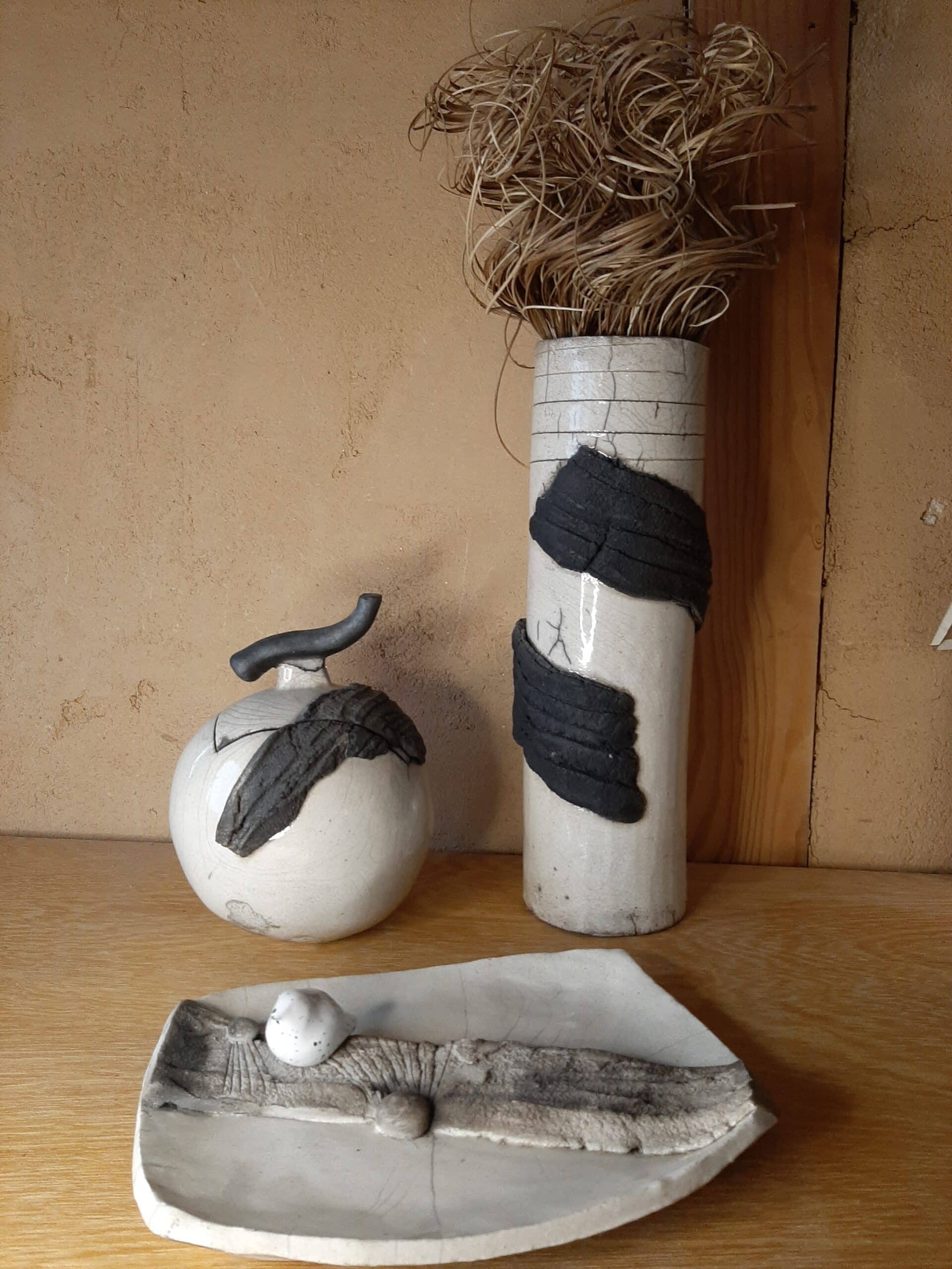 3 poteries blanche et noire sur fond de bois. On voit un partie noire en surepaisseurs. L'une est en forme de boule, l'autre de vase tout long et la derniére est un vide poche.